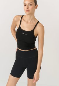 Czarny prążkowany top na ramiączkach o skróconym fasonie z małym logiem na środku, zestawiony z czarnymi rowerowymi szortami o wysokim stanie.