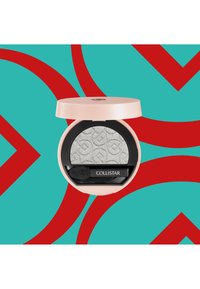 Poudre compacte ronde avec un couvercle rose pâle et une base noire, contenant un fard à paupières argenté texturé. Comprend un petit applicateur. Fond abstrait turquoise et rouge.