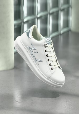 Weiße Leder-Sneaker mit silbernen Akzenten, auffälliger Markenkennzeichnung, runder Zehenpartie und Schnürverschluss. Glatte Textur mit minimalistischem Design.
