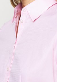 Camicia a collo rosa chiaro con sottili strisce orizzontali, che mostra la parte superiore del petto e due bottoni chiusi.