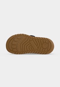 Semelle d'une chaussure d’enfant en caoutchouc marron avec des motifs, le mot "barefoot," et la taille 25 visibles.