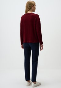 Gebreide bordeauxrode trui met een losse pasvorm en verlaagde schouders, gecombineerd met marineblauwe slim-fit broek en witte sneakers.