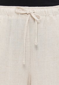 Linen hlače v off-white barvi z teksturirano površino. Imajo elastičen pas in vrvico za nastavljanje fit.