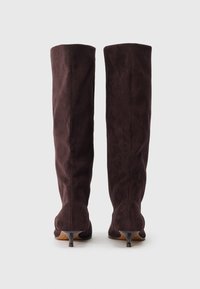 Knee-high boots in dark brown suede with a fitted design, pointed toe, and a small heel. Smooth texture with no visible embellishments.