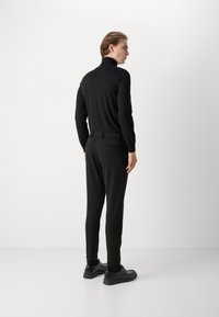 Men's black turtleneck sweater and tapered black trousers, featuring a smooth texture and fitted design, paired with black dress shoes.