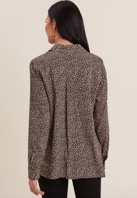Chemise à manches longues à motifs léopard en tan et noir, avec un col, au style décontracté. Tissu doux avec une texture lisse.