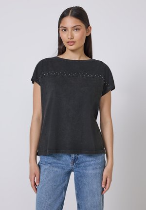 Top negro de manga corta con escote redondeado, tejido texturizado y tachuelas decorativas en la parte superior del frente. Combinado con jeans de color azul claro.