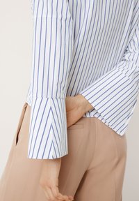 Randig skjorta med blå och vita vertikala ränder, med lång ärm och något utvikt manschett samt en mjuk bomullstextur.