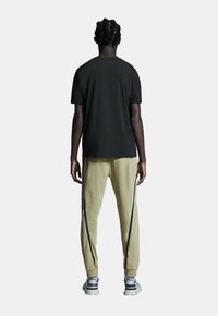 Sort bomulds T-shirt med korte ærmer, parret med lysegule sweatpants med sidelommer og grå sneakers med sorte accenter.