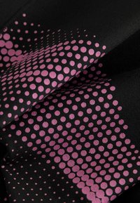 Svart textil med en gradient av cirkulära rosa prickar i olika storlekar, med en texturerad yta. Tygets veck skapar mjuka skuggor.