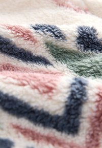 Tissu doux et moelleux avec une surface en peluche texturée couleur crème, présentant des motifs abstraits en forme de feuilles bleu marine, vert et rose poudré.