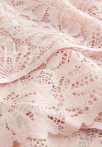 Tela de encaje rosa suave con patrones florales y bordes con ondas, que muestra un trabajo calado delicado y una textura fina.