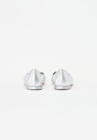 Ballerines en métal argenté avec une texture lisse, un bout rond, un petit talon, et des détails de couture à l'arrière, sur fond blanc.
