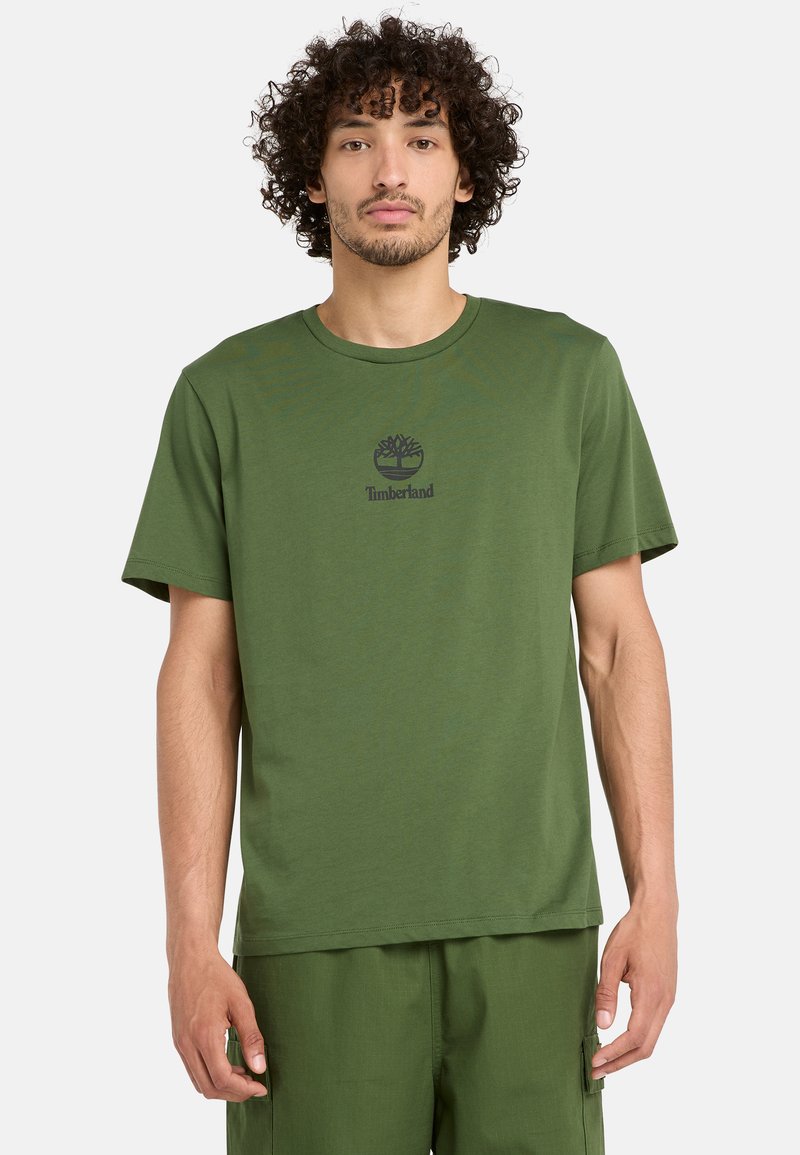 Grön bomullströja med korta ärmar, rund halsringning, med en mörk logotyp ovanför bröstet. Mjuk textur, avslappnad passform, enkel design.