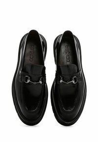 Mocasines de cuero negro con punta redondeada, acabado brillante, herrajes metálicos decorativos y una banda texturizada en el empeine.