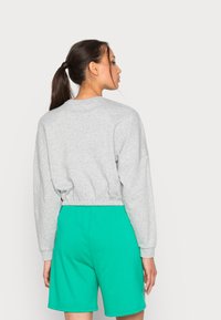 Sudadera gris corta con mangas largas, cintura elástica, combinada con pantalones cortos verdes. Tejido de algodón, corte relajado, diseño simple.