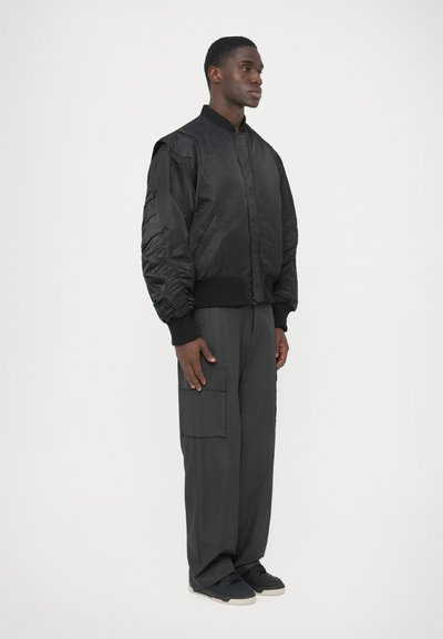 Juoda bombonešio striukė su ribota rankogaliais ir apykakle, su pūstomis rankovėmis. Derinama su laisvais pilkais krovinių kelnėmis ir juodais sportbačiais.