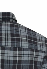 Col de chemise à carreaux noir et gris avec des lignes contrastantes bleu clair et blanches ; tissu texturé avec un motif de trame visible.