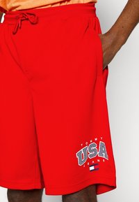 Rode mesh shorts met een elastische tailleband, voorzien van zijzakken en een "TOMMY USA JEANS" graphic in het wit. Inclusief een kleine vlagaccent.