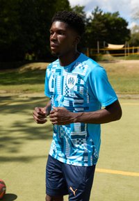 Tricou sportiv albastru cu un model geometric, având guler rotund și mâneci scurte, asortat cu pantaloni scurți bleumarin și accente portocalii.