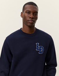 Sötétkék pulóver, puha anyagból készült. Kerek nyakú, bal mellrészen világoskék hímzett LD logóval.