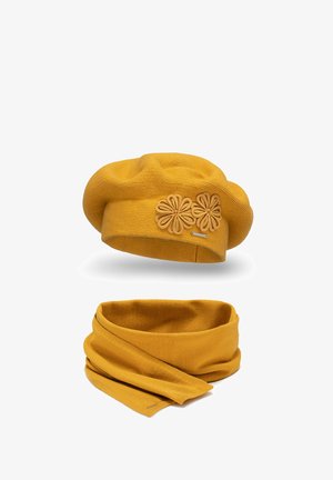 Mosterdgele baret met bloemenschema van leer en een bijpassende infinity-sjaal, beide gemaakt van zachte, gestructureerde gebreide stof.