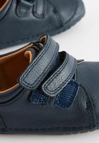 Blå läderskor med texturerade detaljer och kardborreband. Rundad tå och sydda detaljer på sulan. Inredningen har en beige foder.