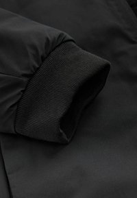 Manche en tissu noir avec un poignet tricoté en côte, montrant la texture et les détails de couture sur un matériau lisse et froncé.