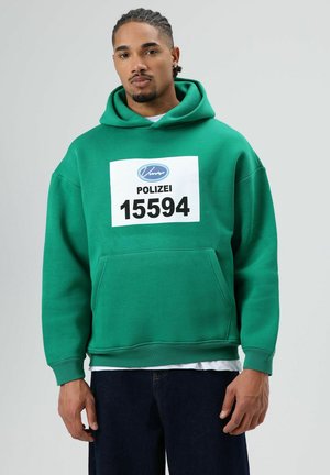 Groene hoodie met een grote voorzak, voorzien van een witte bedrukte label met de tekst "POLIZEI 15594". Zachte textuur en een ontspannen pasvorm.