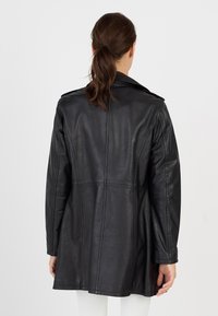 Schwarze Lederjacke mit taillierter Silhouette, langen Ärmeln und Reverskragen. Mit Nahtdetails und glatter Textur.