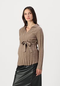 Beige geripptes Umstandssweatshirt mit Kragen, Bindegürtel und langen Ärmeln; kombiniert mit einem schwarzen Ledrock.