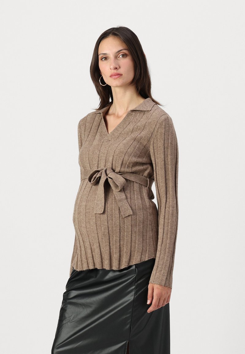 Beige geripptes Umstandssweatshirt mit Kragen, Bindegürtel und langen Ärmeln; kombiniert mit einem schwarzen Ledrock.