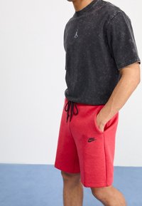 Černé tričko z bavlny s efektom acid-wash a logem Jordan, doplněné červenými bavlněnými šortkami se bočními kapsami a logem Nike. Pas na šňůrku.