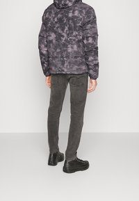 Person som bär en svart och grå acid-wash pufferjacka, mörkgrå slim jeans och svarta högskor som står vänd bort.
