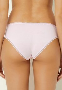 Mutande di cotone rosa con bordo in pizzo ondulato. Hanno un design a vita bassa e una texture liscia. La parte posteriore presenta un aspetto senza cuciture.
