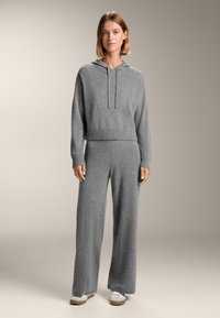 Felpa grigia lavorata a maglia con cappuccio e cordino, abbinata a pantaloni grigi a gamba larga. Texture morbida, vestibilità comoda, adatta per un look casual. Sneakers bianche incluse.