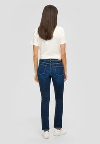 Jean skinny bleu foncé à taille haute, doté de deux poches arrière et d'une texture légèrement décolorée. Associé à un haut blanc à manches courtes.