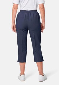 Marineblauwe cropped broek met een elastische tailleband, voorzien van zijsplitten aan de onderrand en gecombineerd met witte sneakers. Gladde stofstructuur.