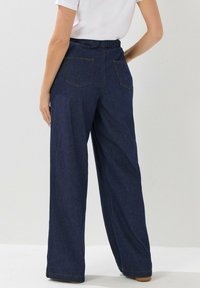Weite Denim-Hosen in Dunkelblau mit strukturierter Oberfläche, ausgestattet mit einem elastischen Bund und zwei Gesäßtaschen.