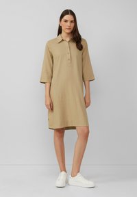 Khaki lněné šaty s knoflíkovou légou, límečkovým výstřihem a tříčtvrtečními rukávy. V kombinaci s bílými teniskami, jednoduchý design.