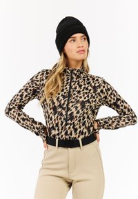 Langärmliges, mit Reißverschluss versehenes Leopardenmuster-Oberteil in Beige und Schwarz, kombiniert mit hoch taillierten beigen Hosen und einer schwarzen gestrickten Mütze.