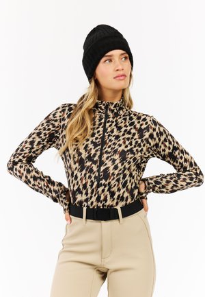 Langermige, met rits gesloten, luipaardprint top in beige en zwart, gecombineerd met hooglopende beige broek en een zwart gebreide beanie.
