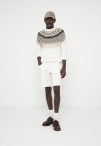 White knit sweater with geometric pattern, white shorts, beige cap, brown shoes, and white socks. Smooth texture and casual fit.