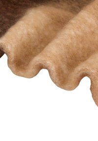 Golvende, tan stof met een zachte textuur, gemaakt van viltwol. Bevat een gelaagd randdetail, dat lichte en donkere tinten mengt.