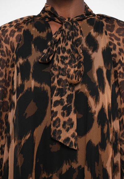 Blusa in chiffon con stampa leopardata marrone e nera, caratterizzata da un dettaglio con nodo al collo e un tessuto fluido che si adagia dolcemente sulle spalle.