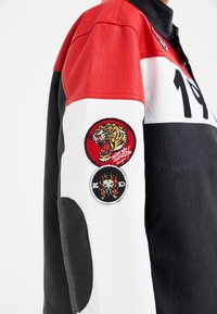 Leather jacket featuring red, white, and black panels. Notable embroidered patches of a tiger and a skull. Textured arm details visible.