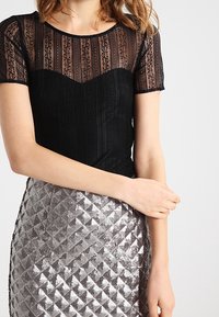 Sort blonderet top med korte ærmer, prydet med et gennemskinneligt stribet design. Kombineret med en skinnende sølvfarvet palietskørt i et quiltet mønster.