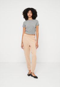 Sivý krátky crop top s krátkym rukávom, béžové tepláky s bočným prúžkom a čierne baleríny; ležérny outfit s mäkkou látkou a uvoľneným strihom.