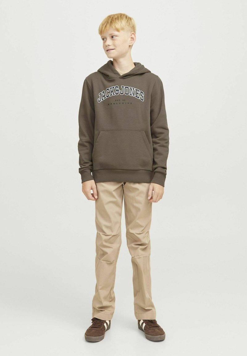 Felpa marrone con tasca frontale e logo, pantaloni beige e sneakers marroni scuri con strisce bianche, modello slim fit, su uno sfondo neutro.