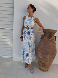 Rochie albă cu imprimeuri botanice albastre, detaliu decupat și o siluetă fluidă. Asortată cu pantofi ascuțiți de culoare albastru deschis, împodobiți cu o piatră prețioasă.